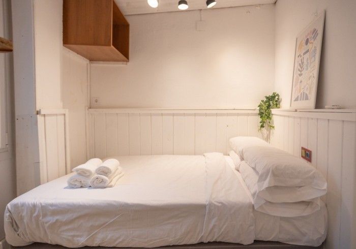 Una cama con sábanas blancas y almohadas en un dormitorio pequeño.