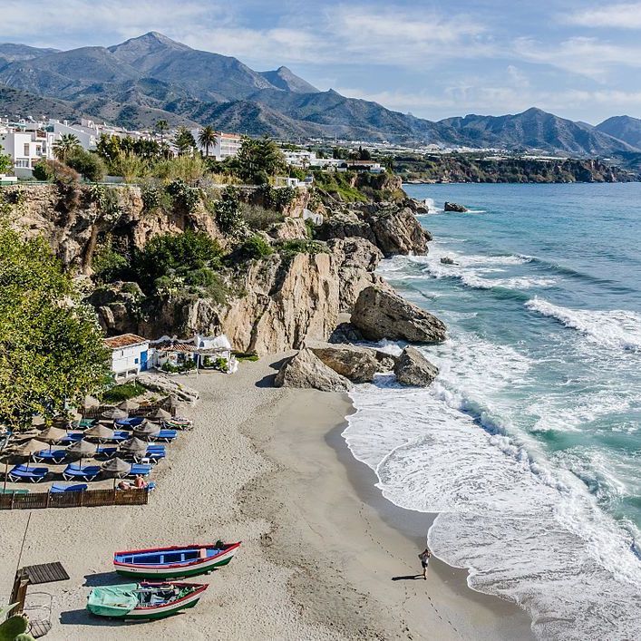 Una playa con barcos y sombrillas y montañas al fondo.