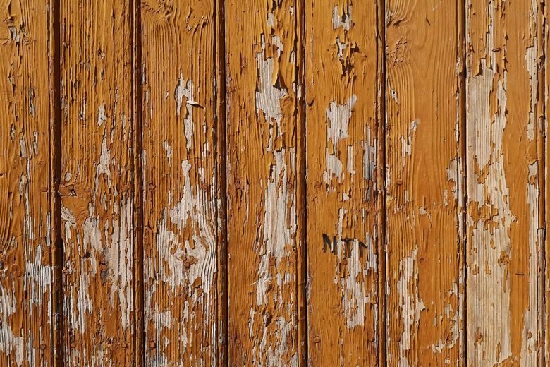 A close up of a wooden wall with peeling paint.