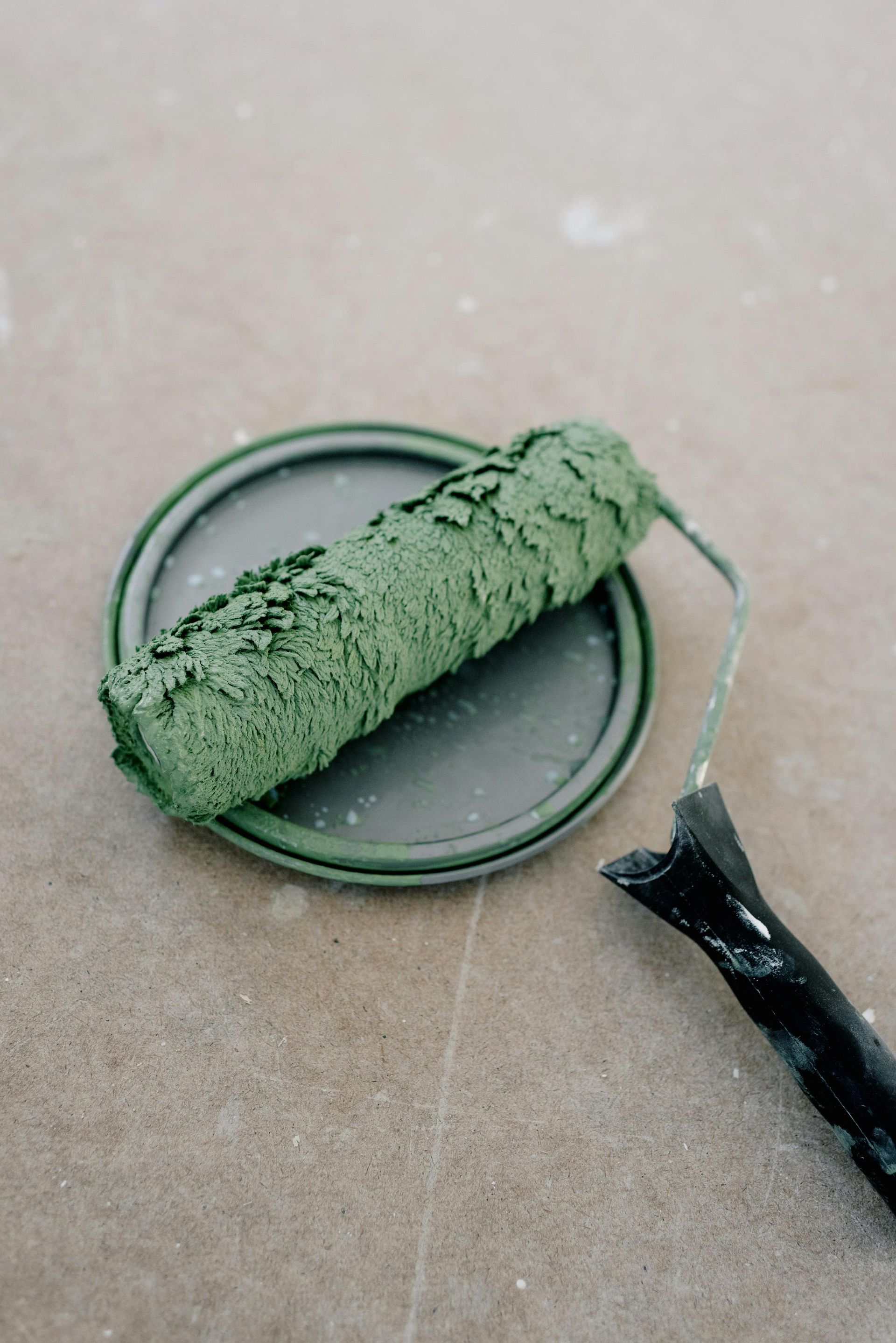 A green paint roller is sitting on top of a paint can.