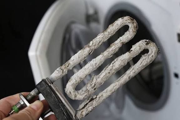 Calcified heating element with heavy mineral buildup from hard water inside a washing machine.