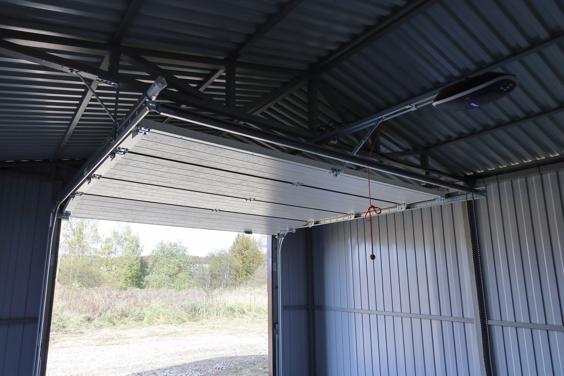 Metal shed interior with open, overhead garage door, visible outdoors beyond the opening.