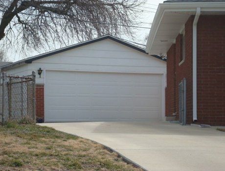 White garage with closed door next to a brick house and a driveway, outdoors.