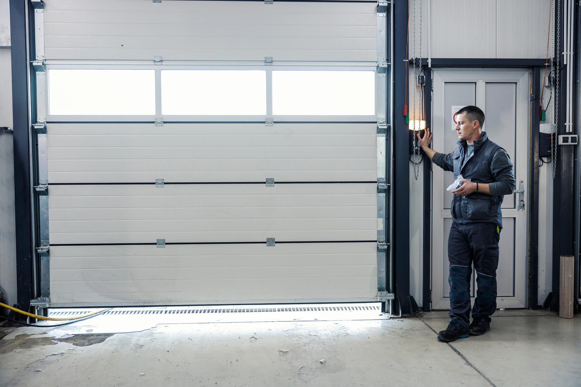 Worker standing by a large gray industrial garage door in a warehouse. Worker standing by a large gray industrial garage door in a warehouse.