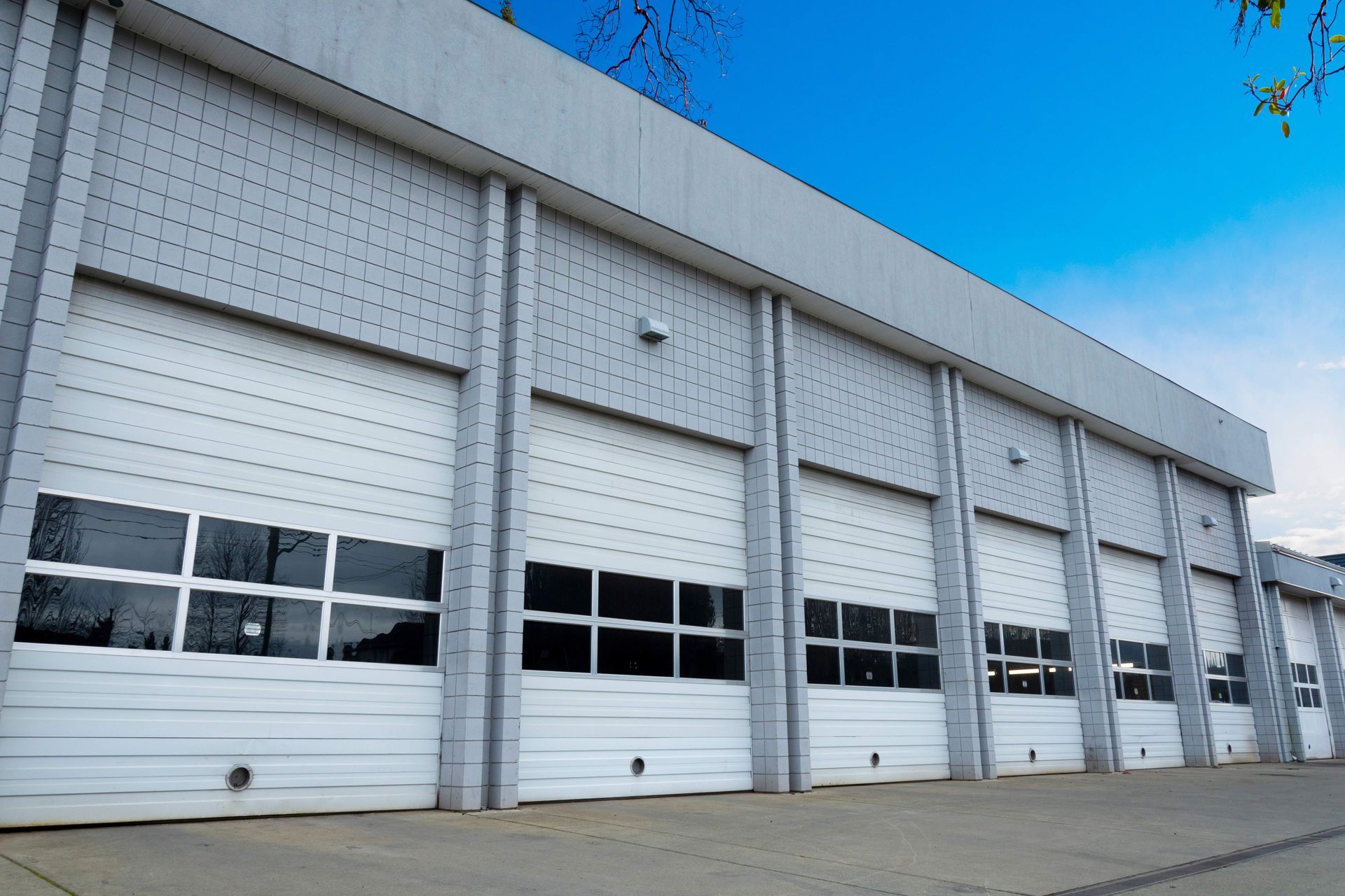Row of white garage doors on a gray building, under a blue sky.