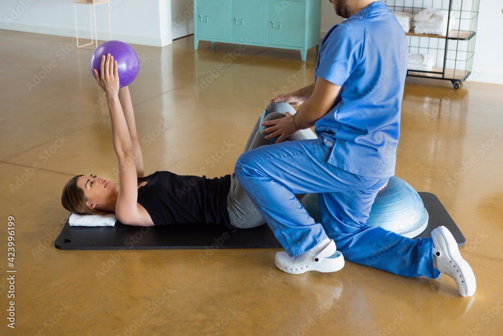 PT working with patient who is holding a purple ball over her head.