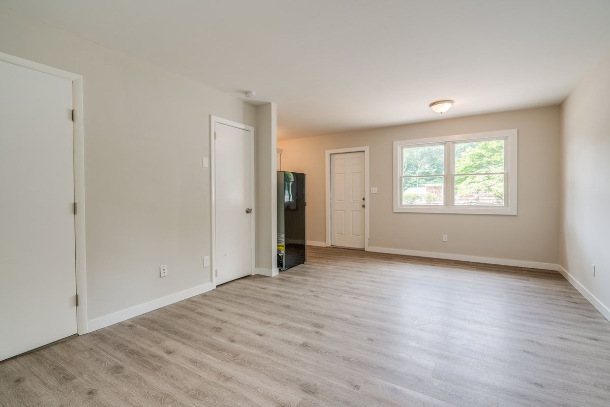 Empty beige bedroom with light wood floors, white doors, and a window letting in daylight