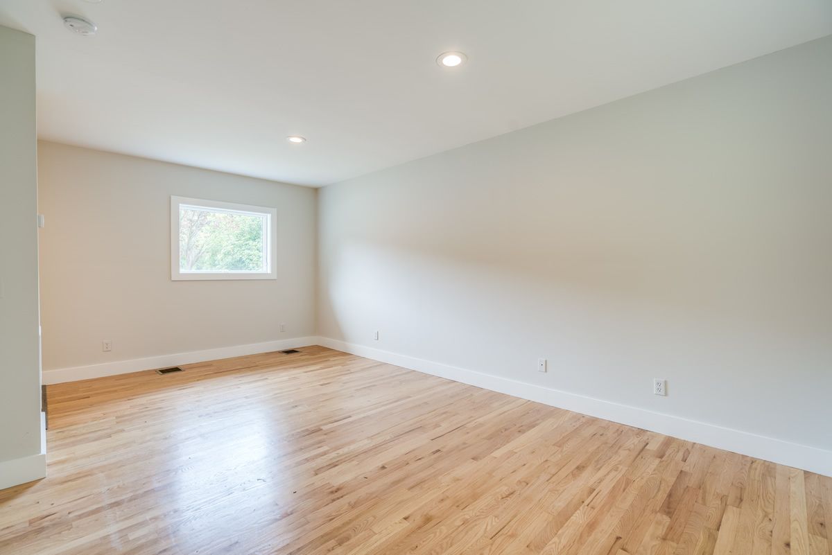 Empty room with light wood floors, white walls, and a small window