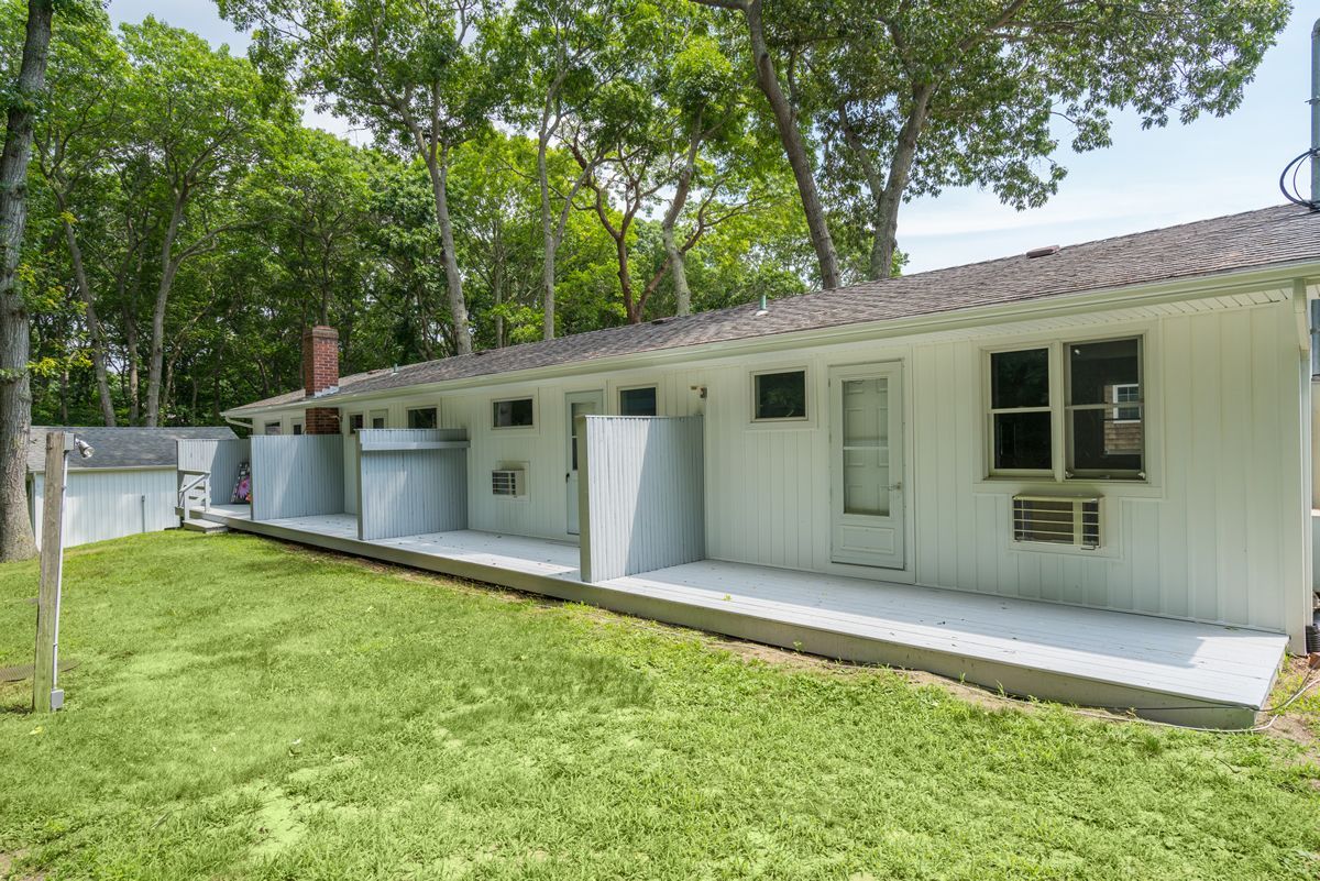 White modular building with a porch and windows beside a grassy yard and trees