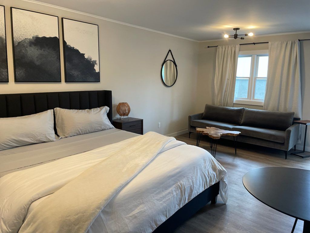 Bright bedroom with a white bed, black headboard, dark couch, and two abstract wall art panels.