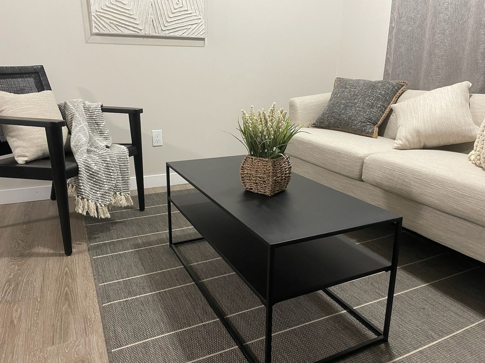 Modern living room with beige sofa, black coffee table, chair, and gray patterned rug