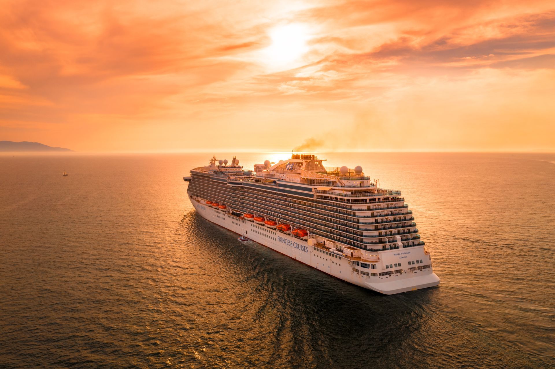 Cruise ship sailing on ocean at sunset, orange sky.