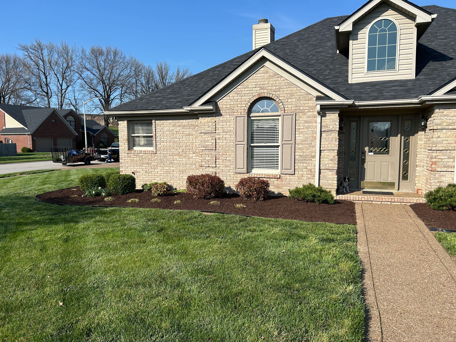 Suburban brick house with a stone facade, front lawn, and walkway on a sunny day