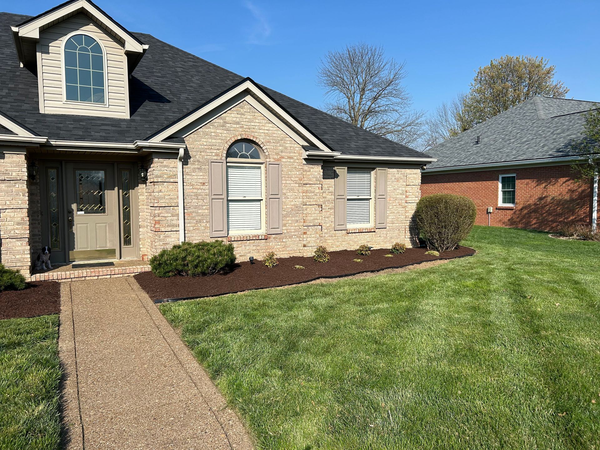 Suburban brick house with stone facade, front walkway, and green lawn under a clear sky
