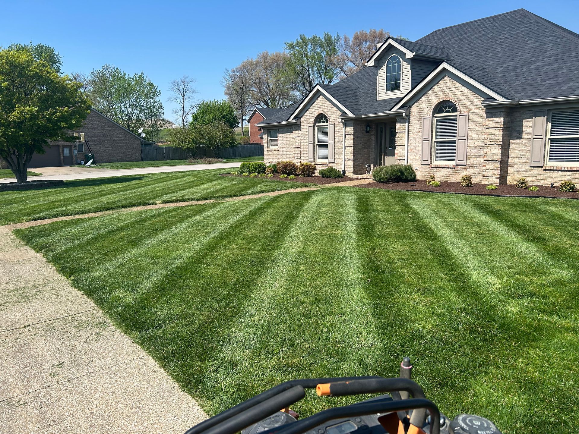 Freshly mowed green lawn beside a stone house under a clear blue sky