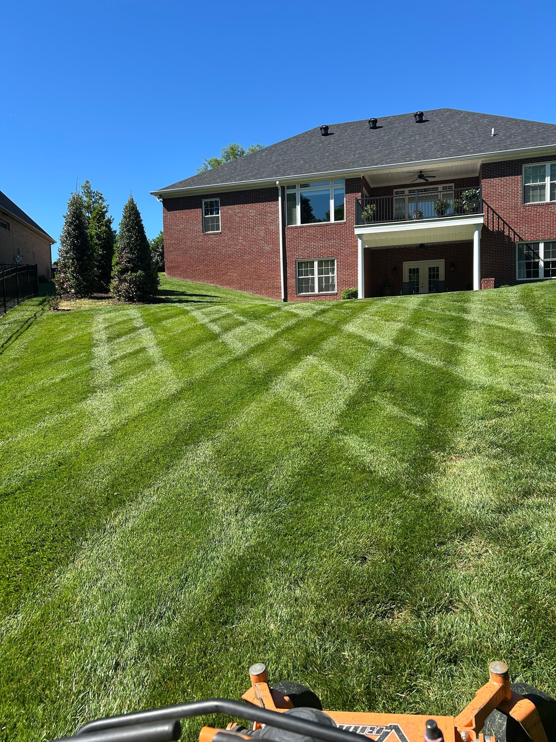 Freshly mowed backyard lawn leading to a brick house on a bright sunny day
