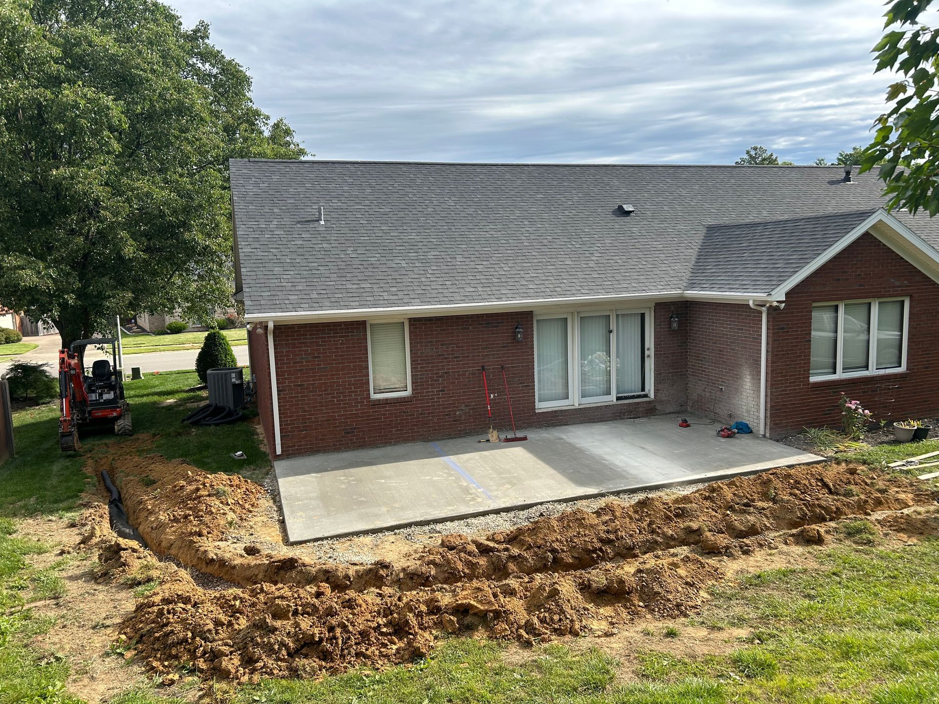 Brick house with a new concrete patio and excavated dirt yard in front