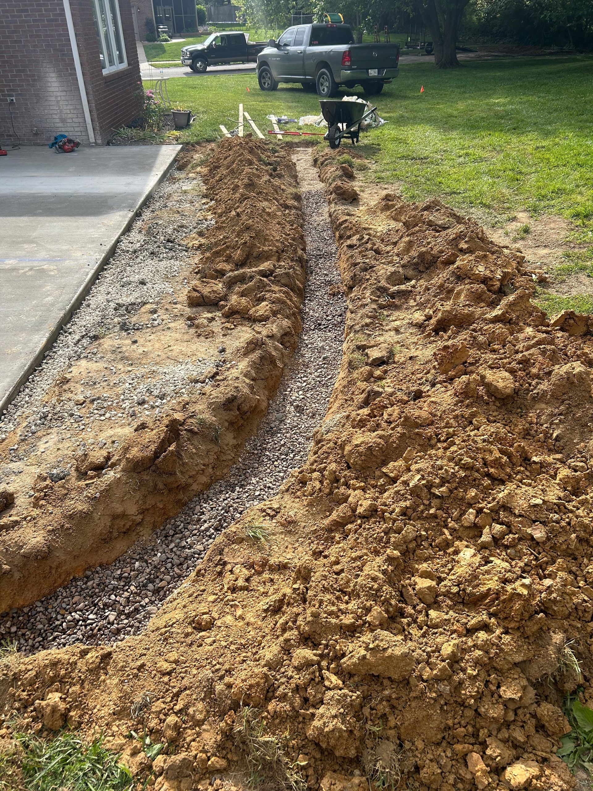 Freshly dug trench filled with gravel beside a house, with loose soil piled along the edge