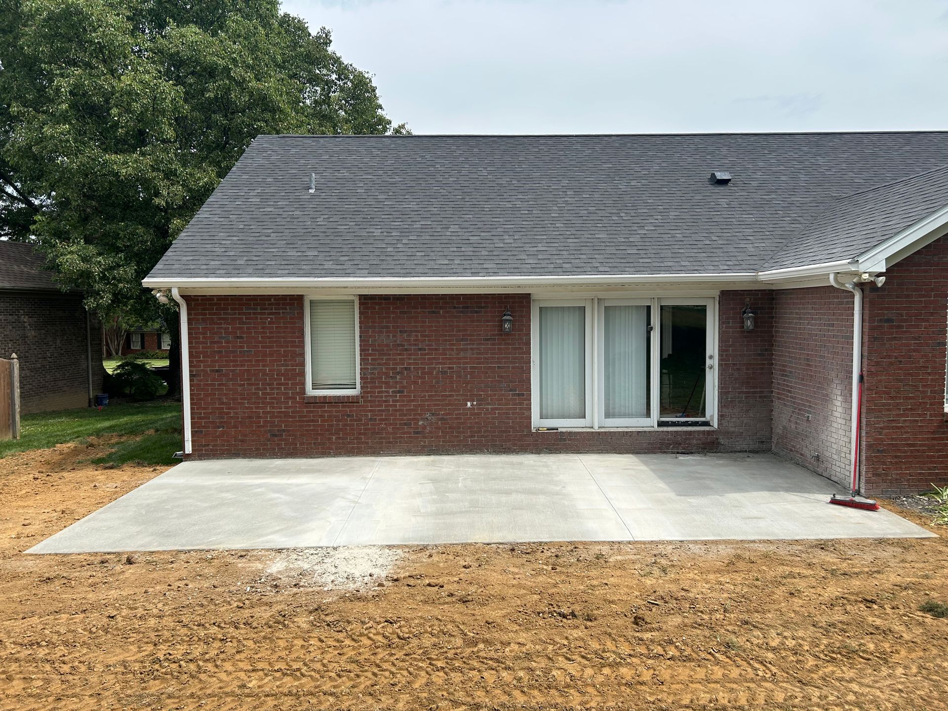 Back patio with concrete slab beside a red brick house and gray shingled roof