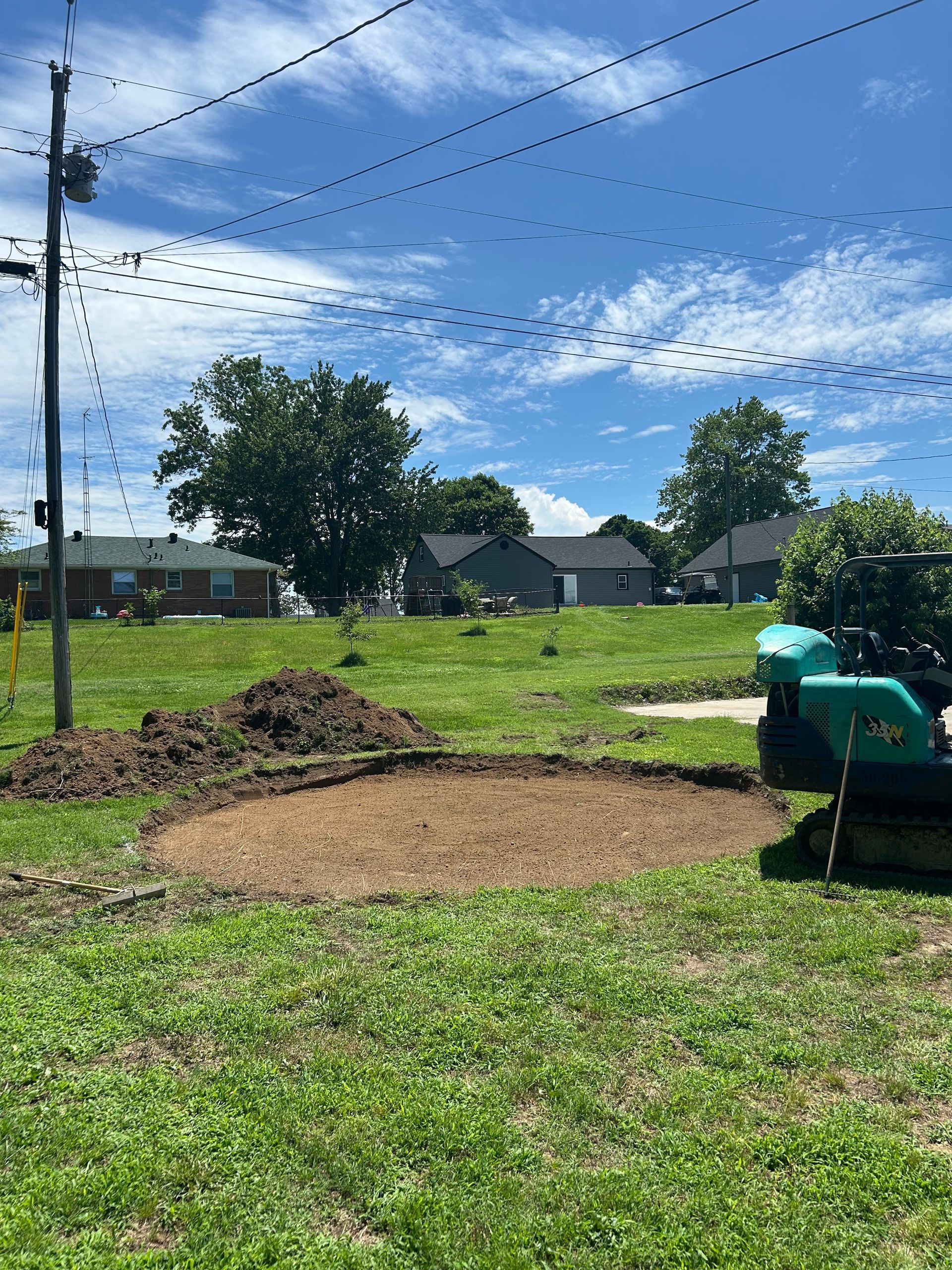 Freshly dug garden bed beside a grassy yard under a blue sky, with a green machine on the right.