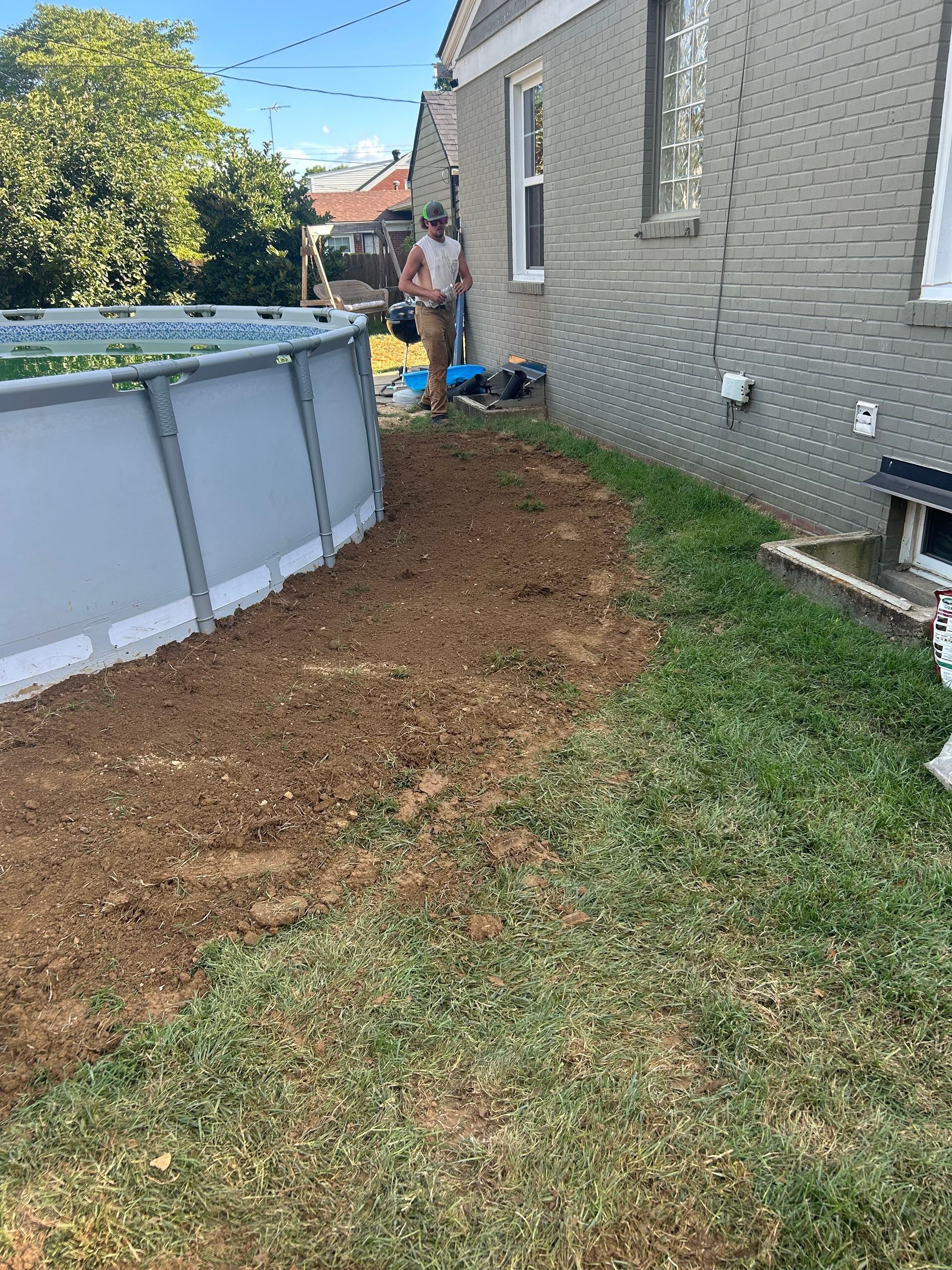 Backyard beside gray house with above-ground pool and fresh mulch path along the side yard