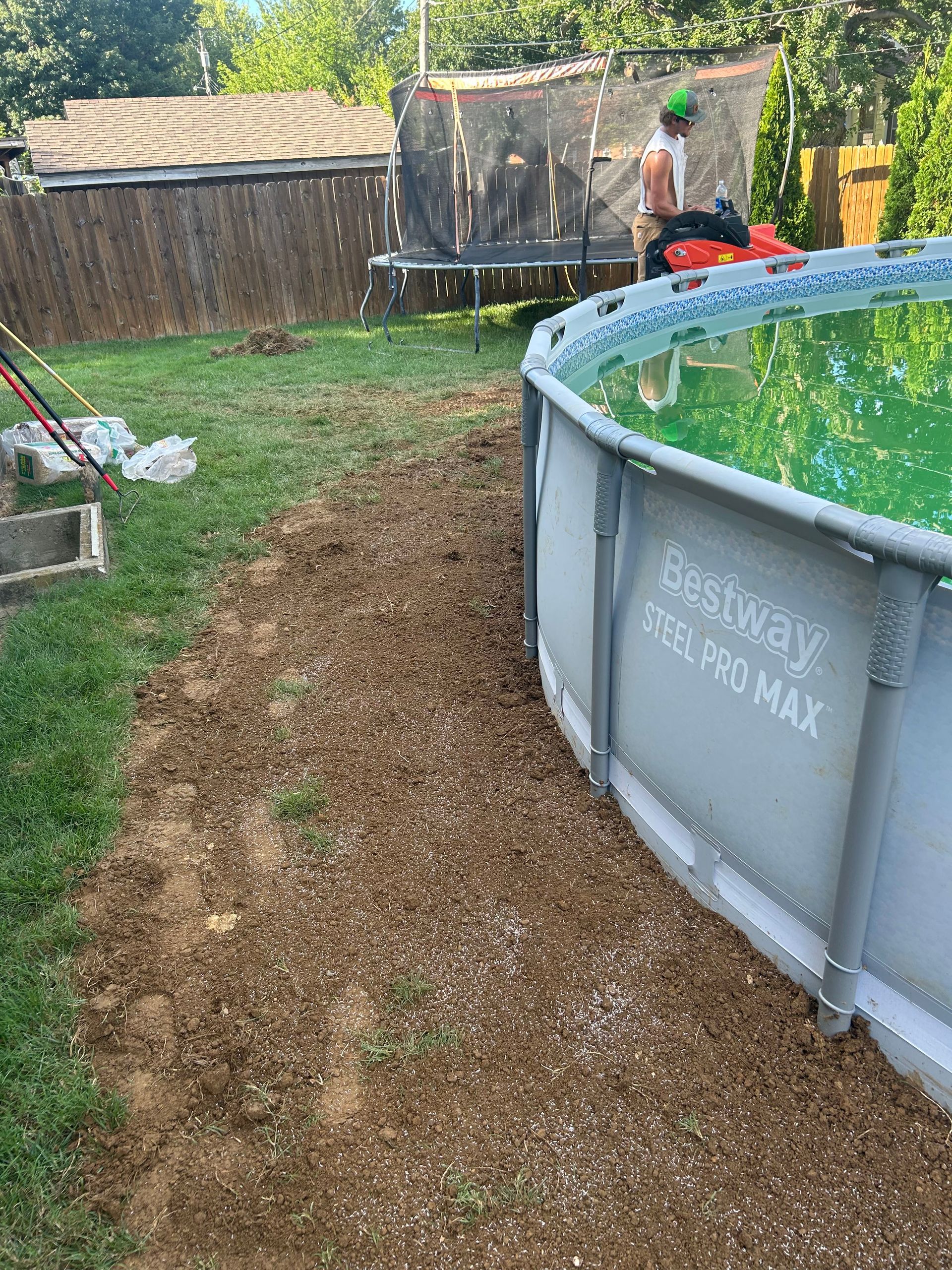 Backyard with an above-ground pool, wooden fence, and a person near the far side of the yard