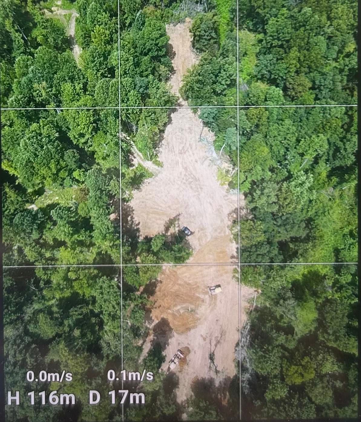 Aerial view of a forest clearing with a muddy, exposed dirt path cutting through dense green trees.