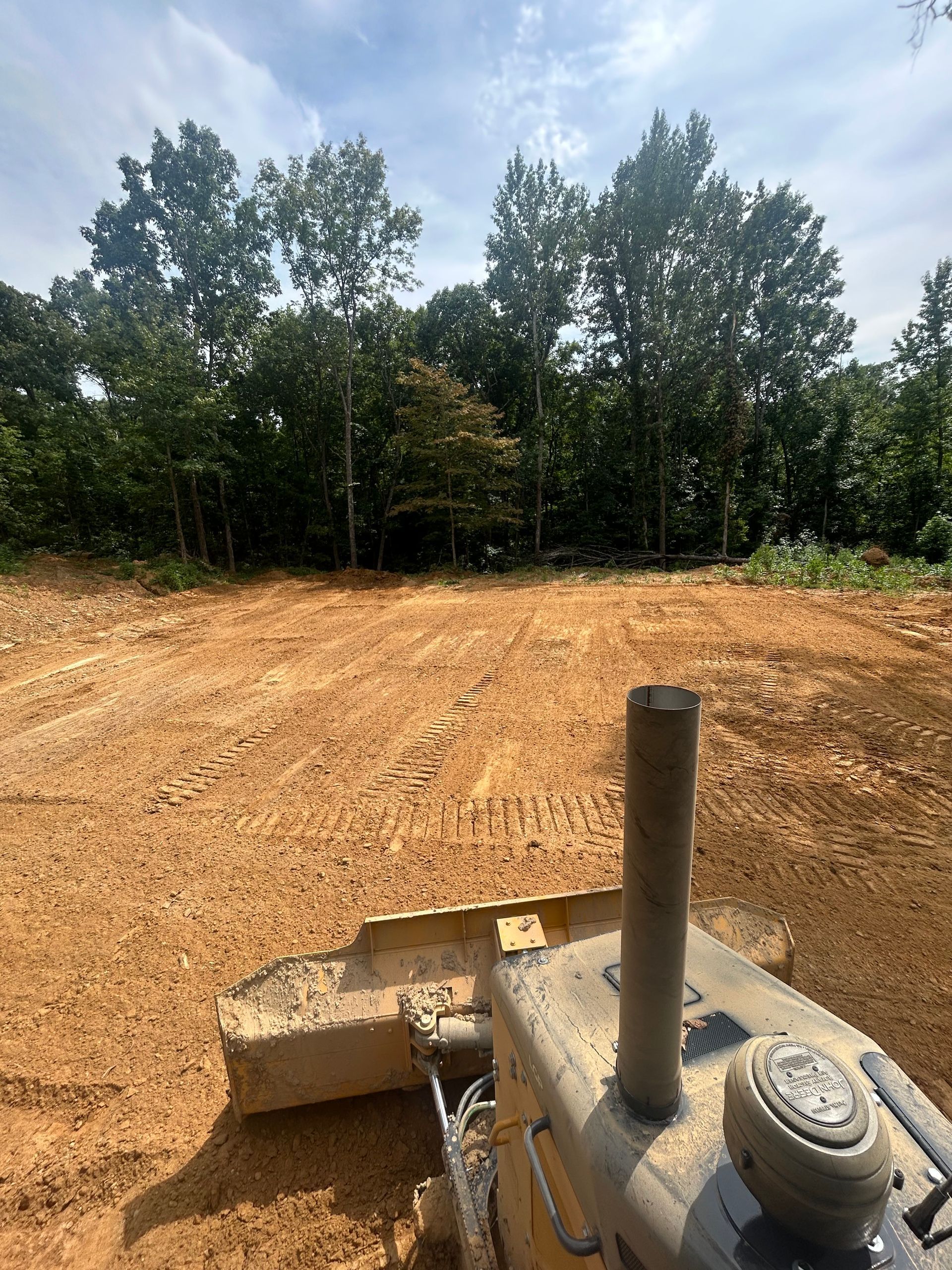 Construction site with dirt clearing, trees in the background, and excavator parts in the foreground