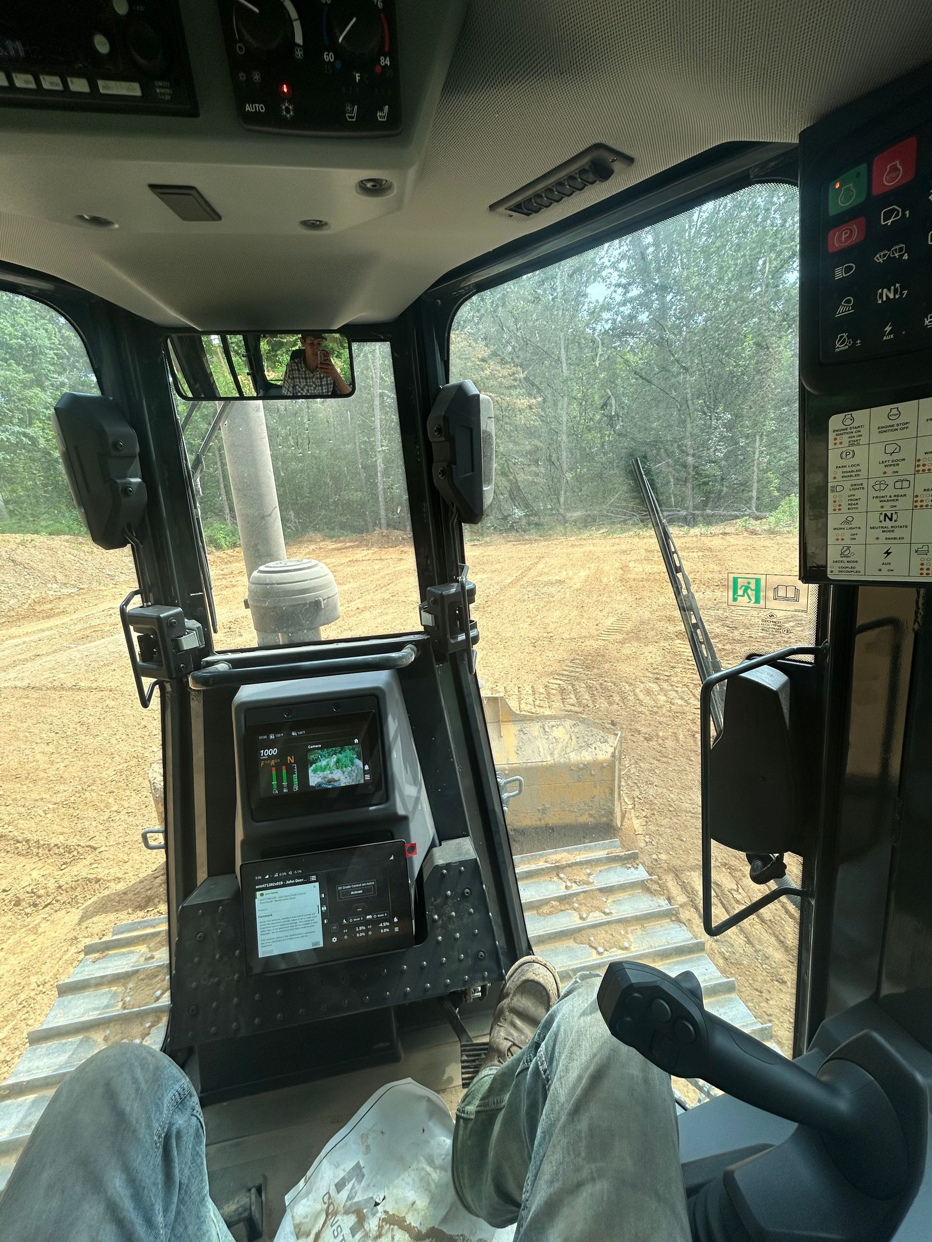 Cab of a construction vehicle with muddy windshield and controls, looking out at dirt worksite.