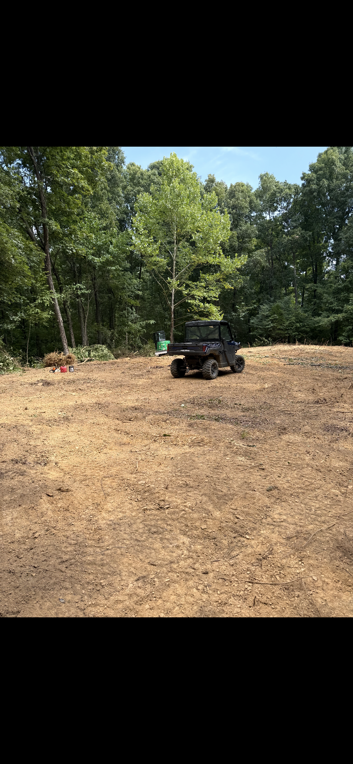 Black ATV parked on a dirt clearing beside trees under a bright sky