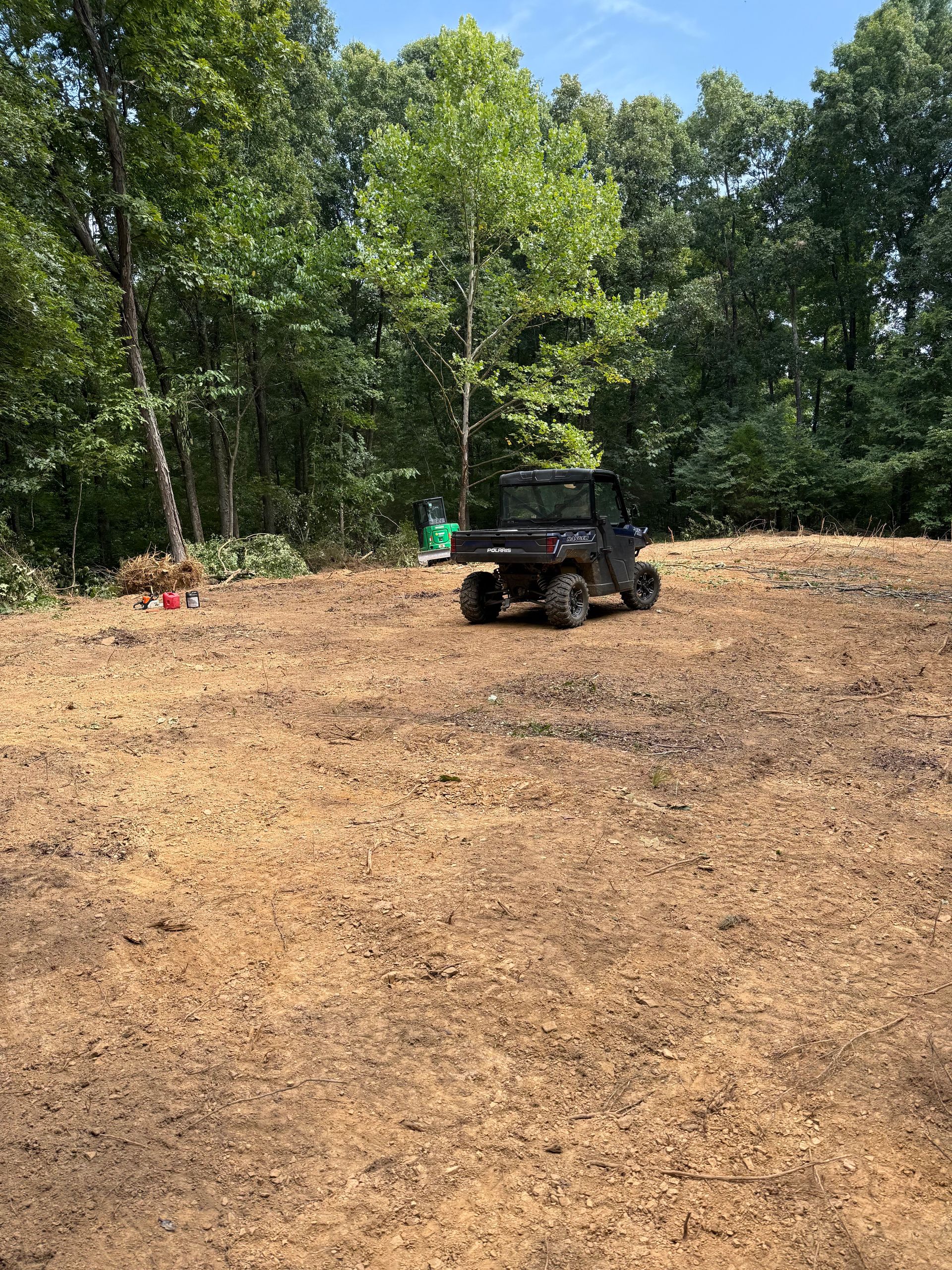 ATV parked on a dirt clearing beside a wooded area, with a person in green nearby.