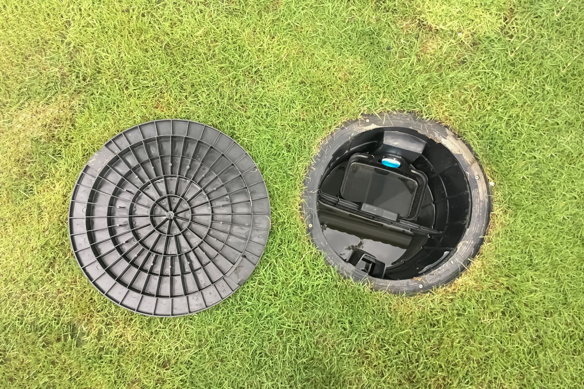 Two open round utility covers in green grass, one closed and one revealing equipment inside