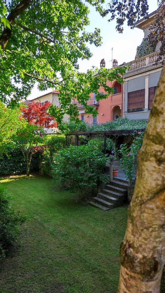 Rigoglioso cortile con giardino, una scalinata in pietra, una casa rosa e alberi frondosi in pieno sole