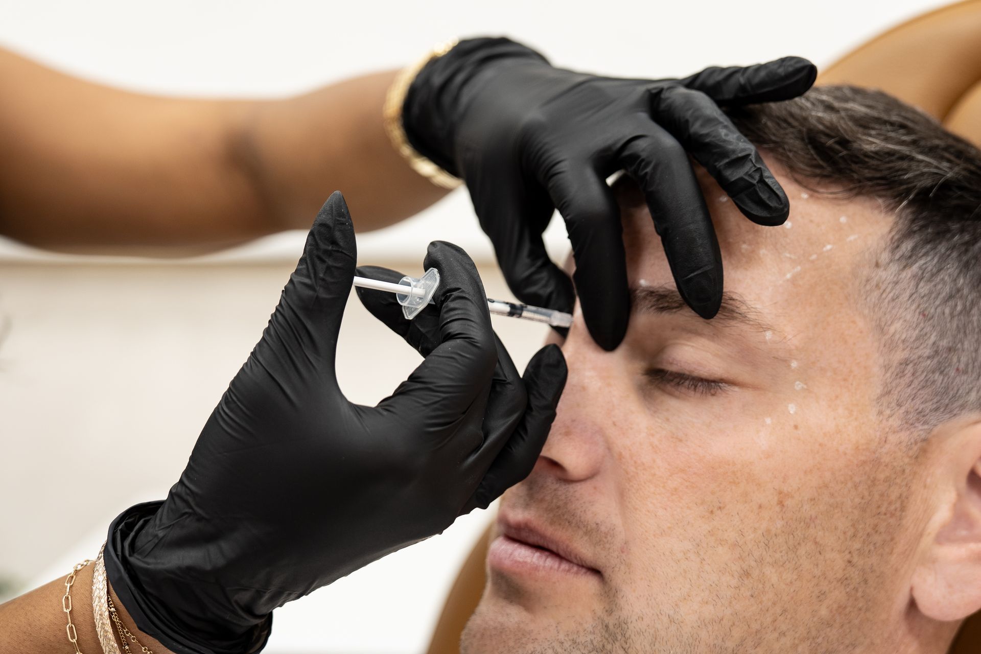 Gloved hands administering a facial injection to a man with eyes closed
