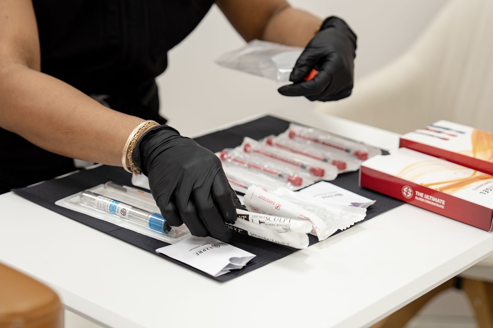Gloved hands sorting packaged syringes and medical supplies on a white table