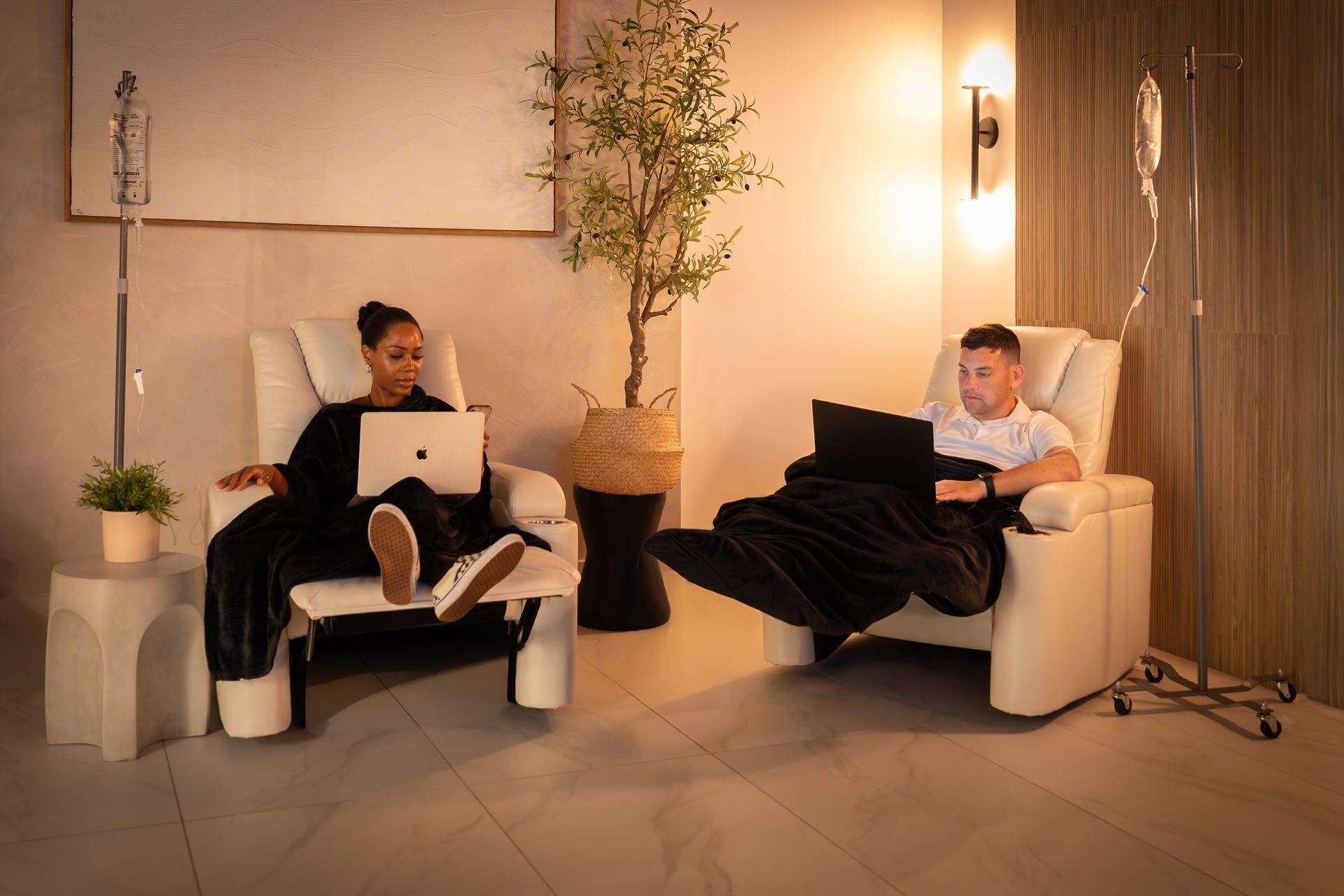 Two people relaxing in black armchairs with laptops in a softly lit modern room