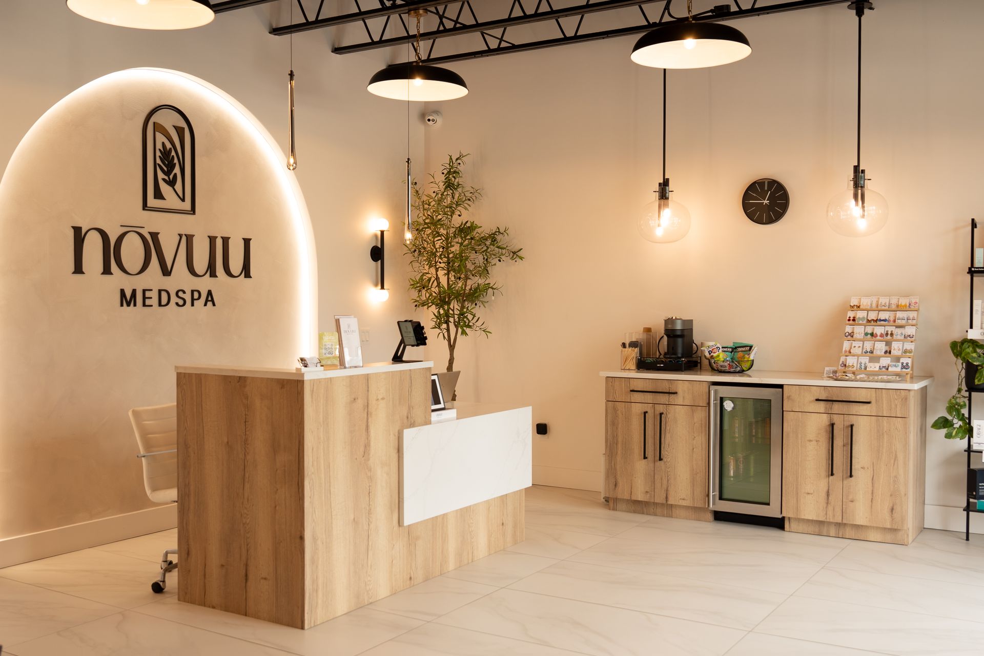 Modern medspa reception area with wood desk, logo wall, and minimalist cabinets under warm pendant lights