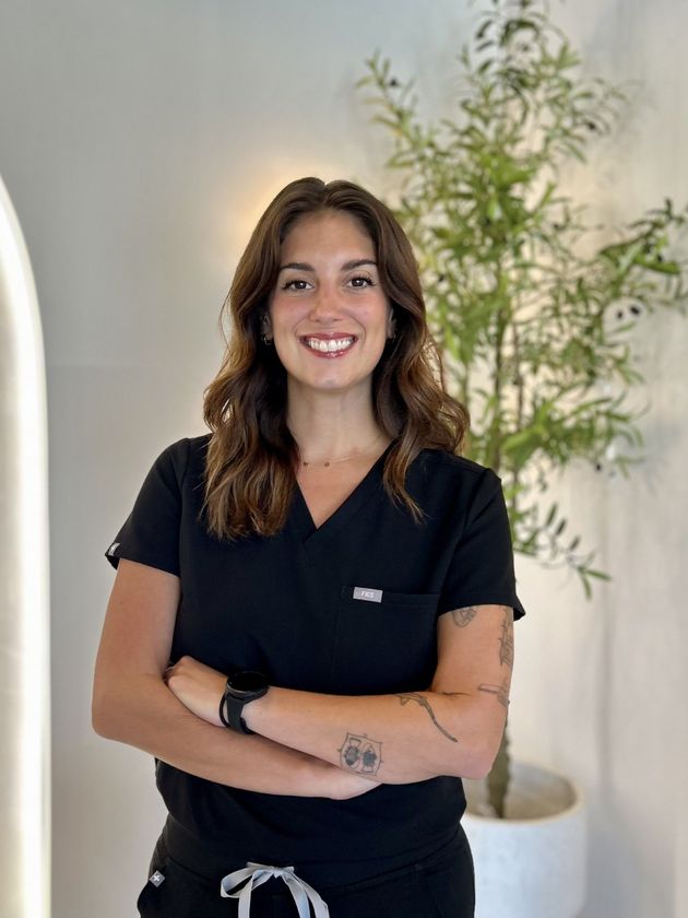 Smiling woman at desk with laptop in a bright office, seated in front of a wall logo.