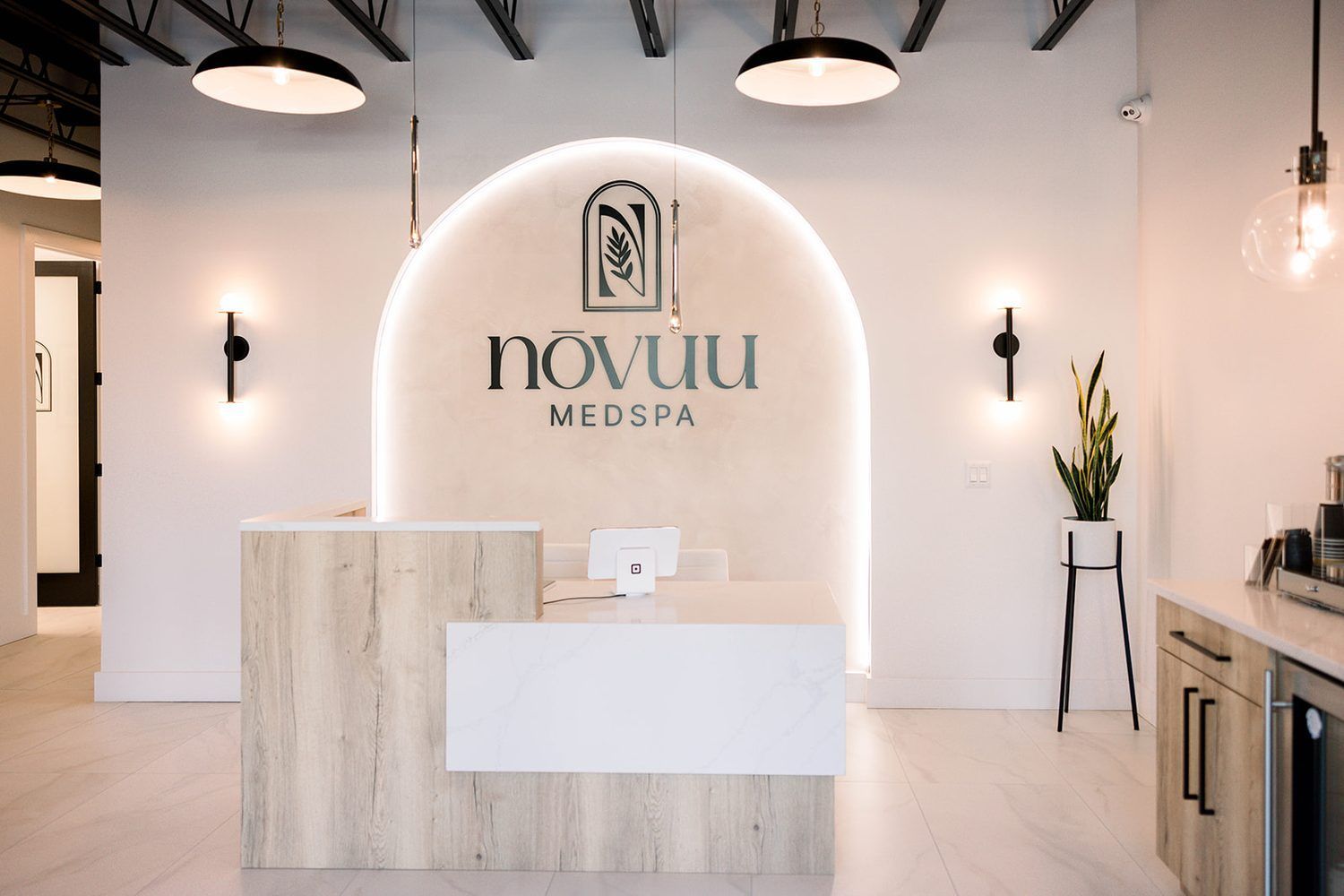 Modern spa reception with white arched wall, wood-and-white desk, and hanging black lights