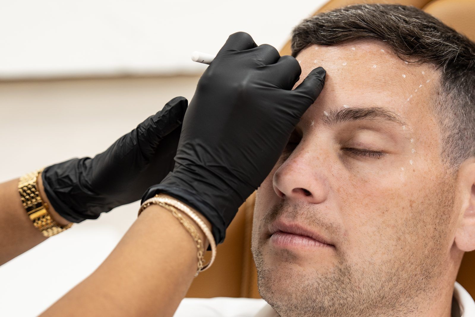 Gloved hands carefully shaping a man’s eyebrow during a cosmetic procedure