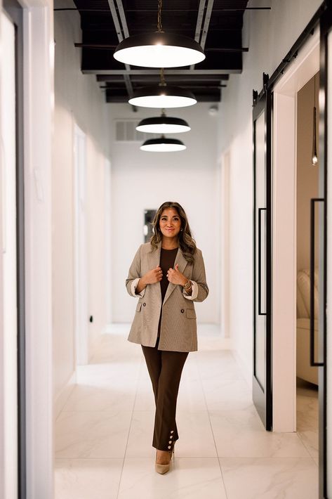 Woman walking down a modern office hallway with white walls, black-framed doors, and hanging circular lights