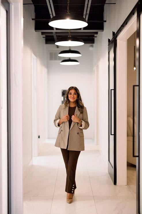 Woman walking down a modern office hallway with white walls, black-framed doors, and hanging circular lights