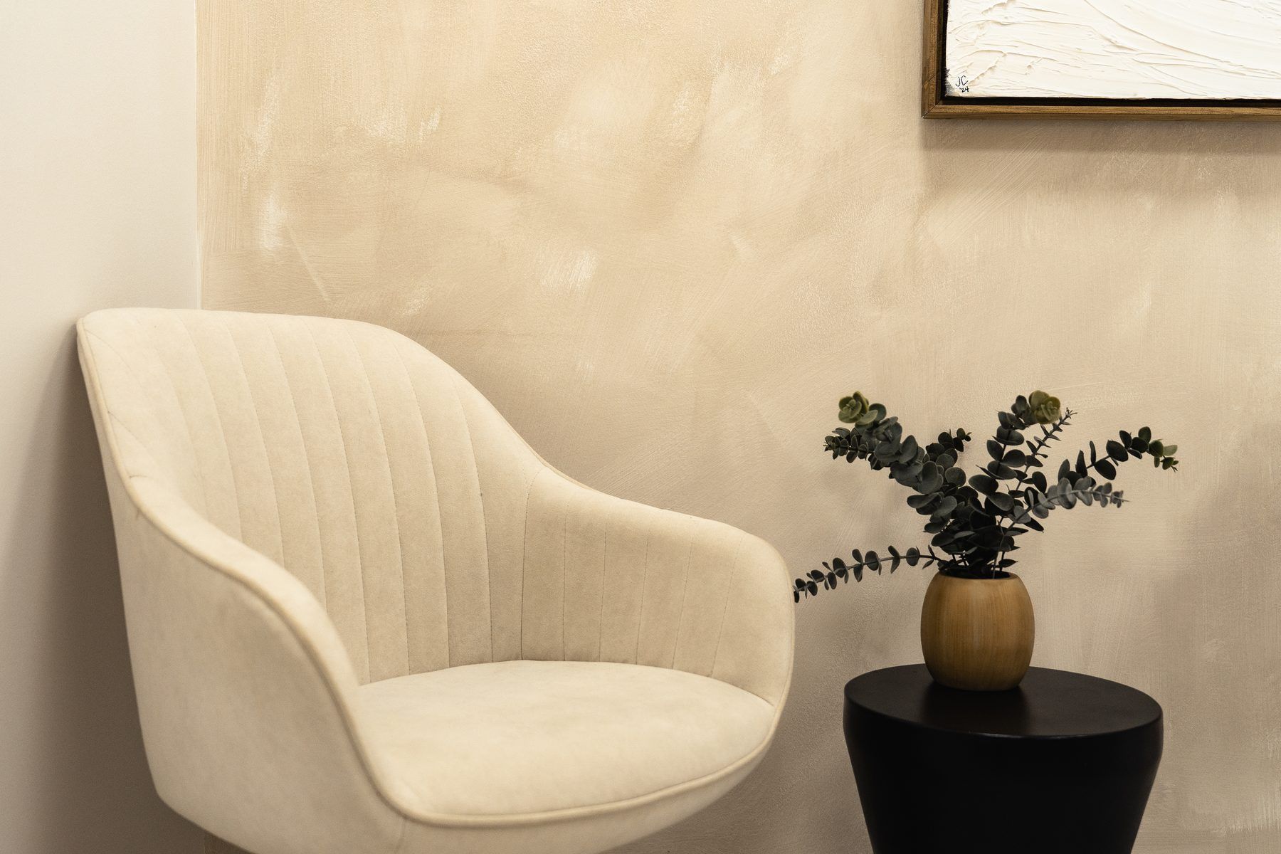 Cream armchair beside a black side table with a potted plant in a beige room
