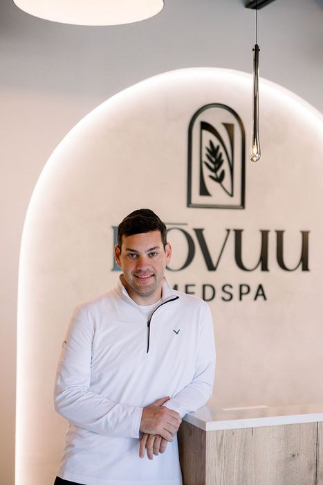 Man standing in a white spa lobby with a “Rovuu Medspa” sign behind him.