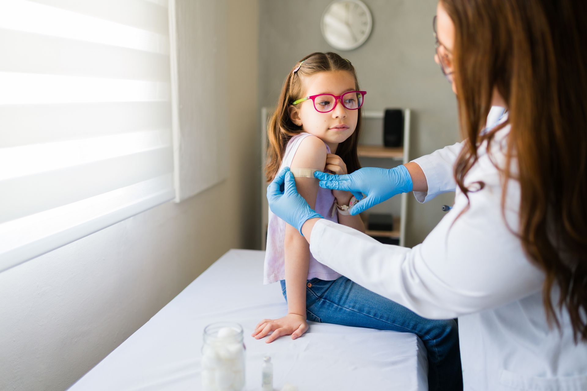 Medical professional applying a bandage after vaccination on a child’s upper arm. Medical professional applying a bandage after vaccination on a child’s upper arm.