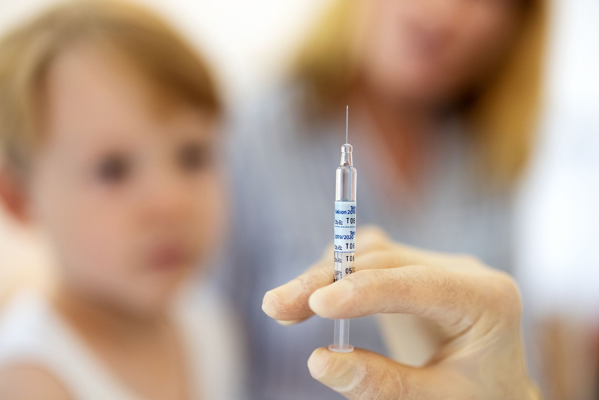 The doctor prepares a vaccine syringe as a young boy waits in the clinic background
