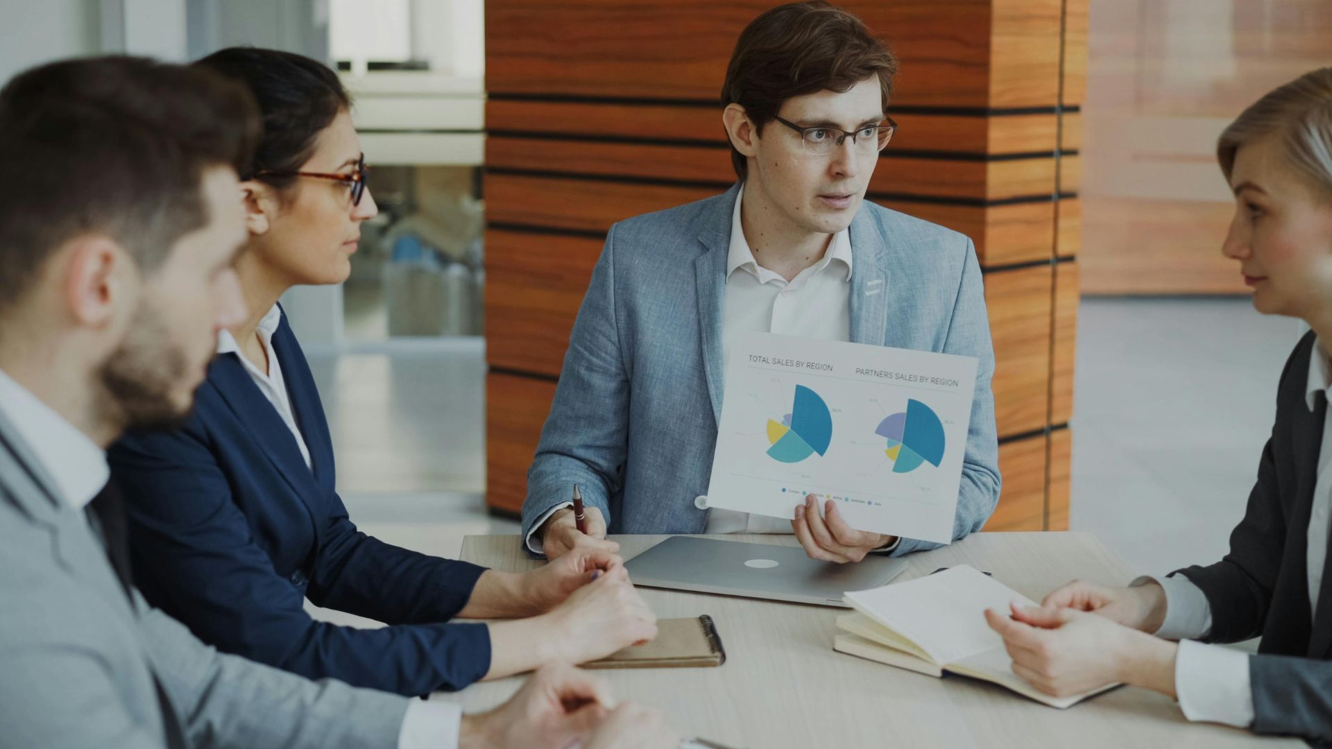 Business meeting with four people reviewing charts and documents around a conference table.