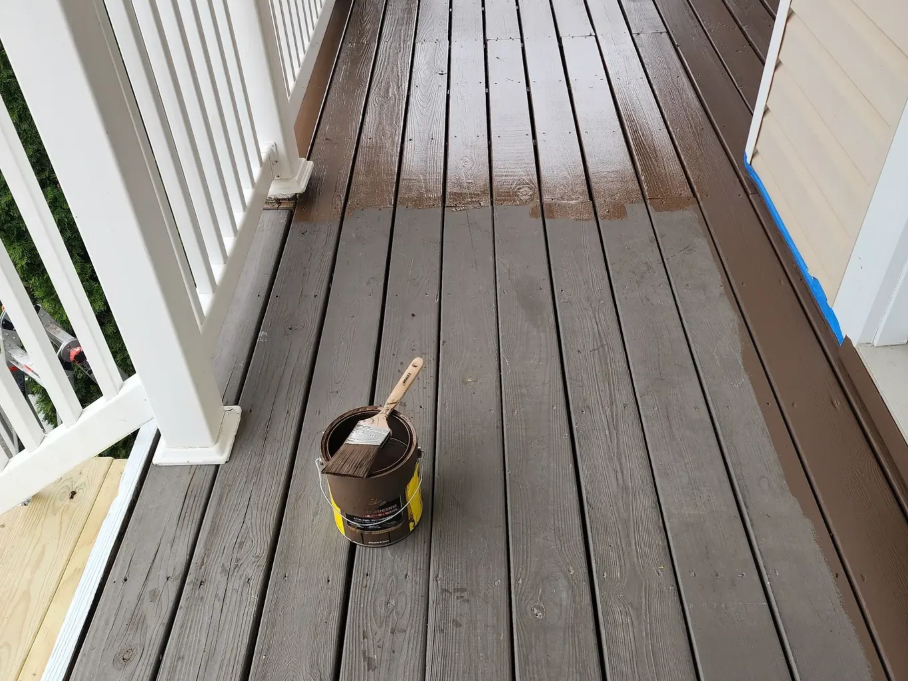 Paint can with brush on a gray wooden porch floor