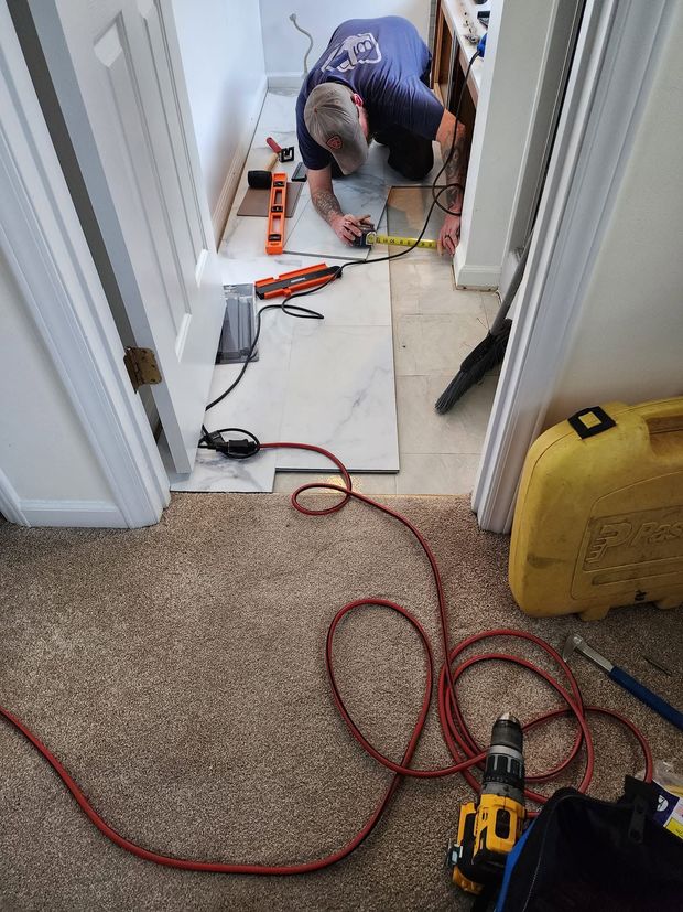 Worker kneeling on a hallway floor, using tools and cables during home repair work.