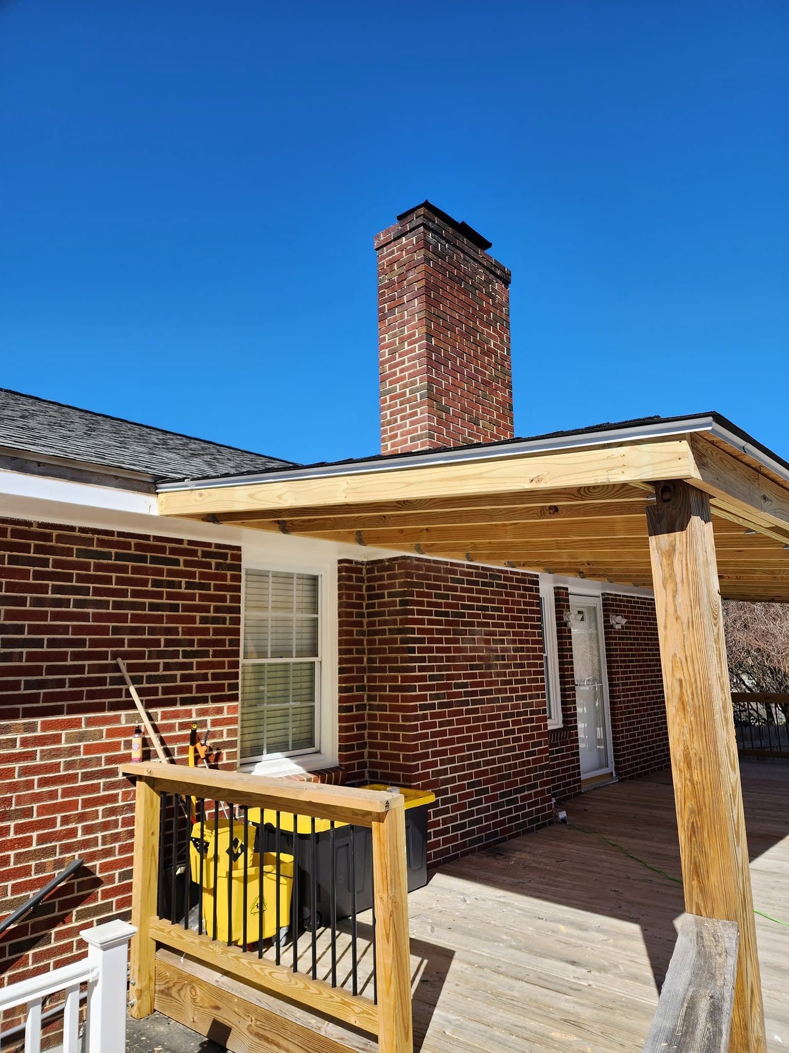 Brick house porch with wooden deck, railing, white door, and chimney under a clear blue sky